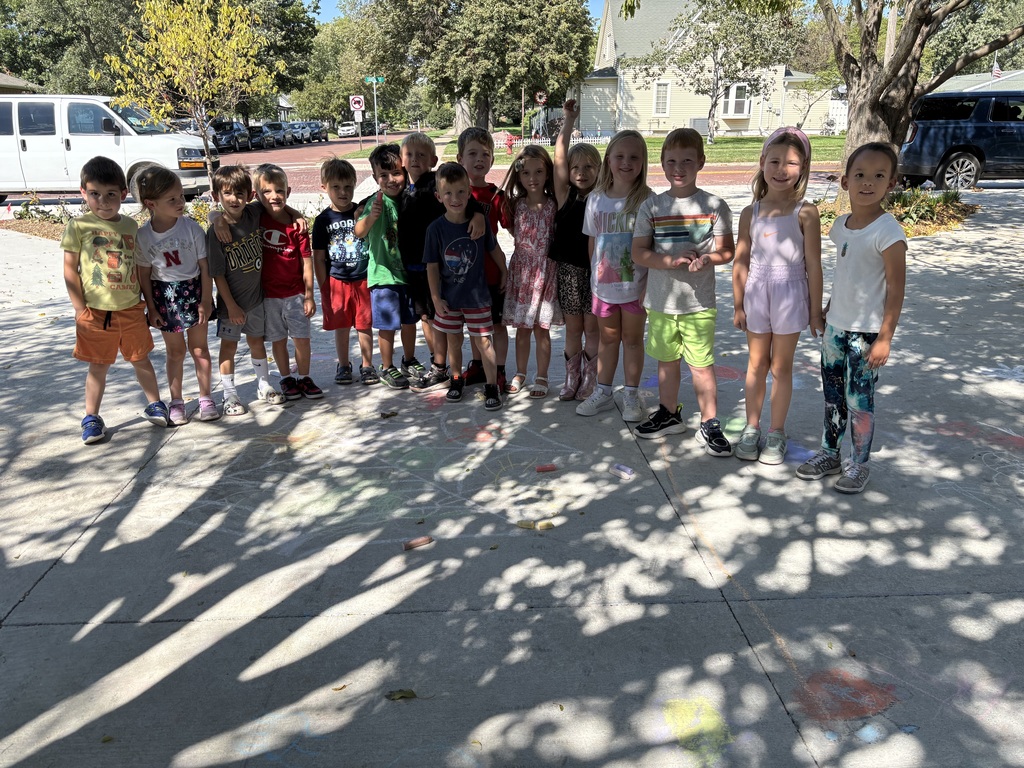 A group of students stand outside on a sidewalk decorated with sidewalk chalk.
