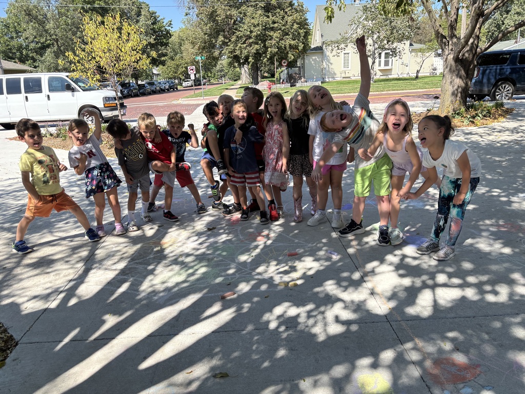 A group of students stand outside on a sidewalk decorated with sidewalk chalk.