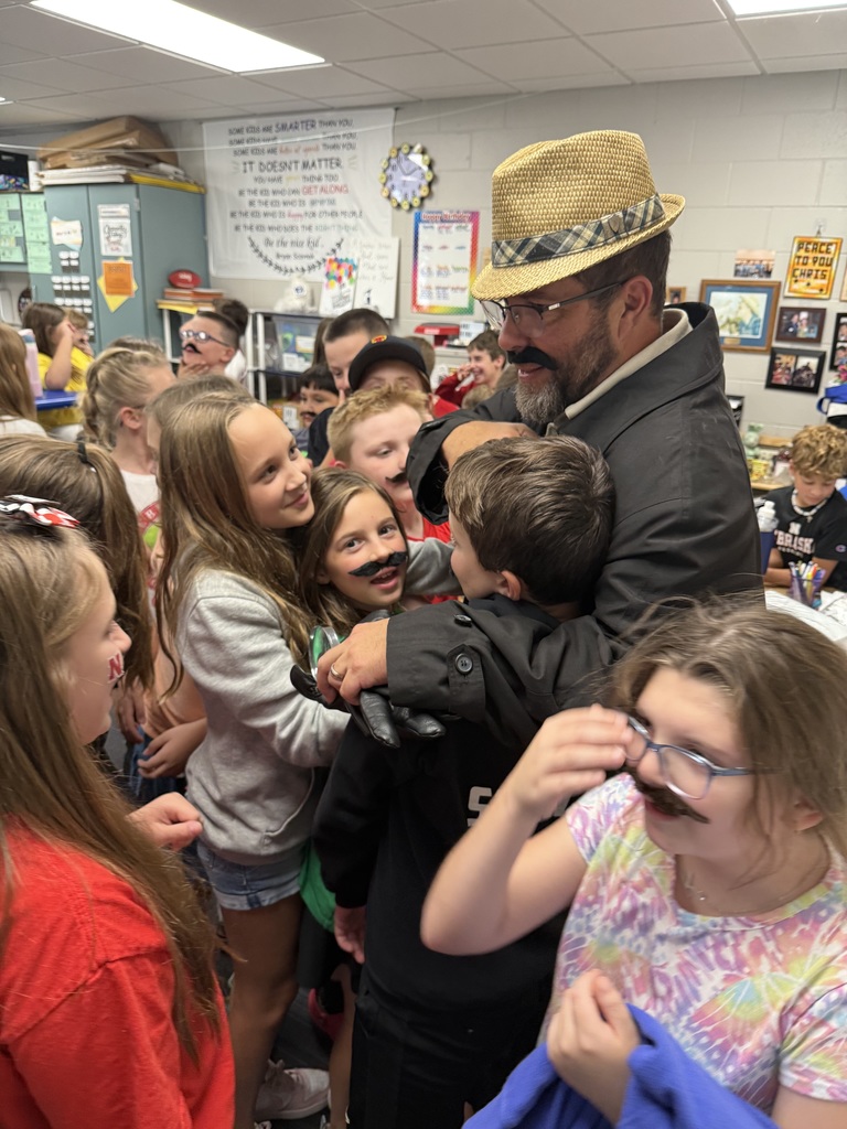 Group of students standing around a man wearing a hat and a fake mustache.
