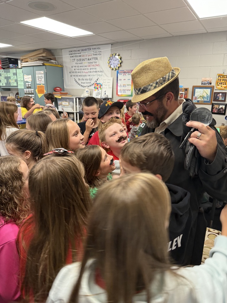 Group of students standing around a man wearing a hat and a fake mustache.