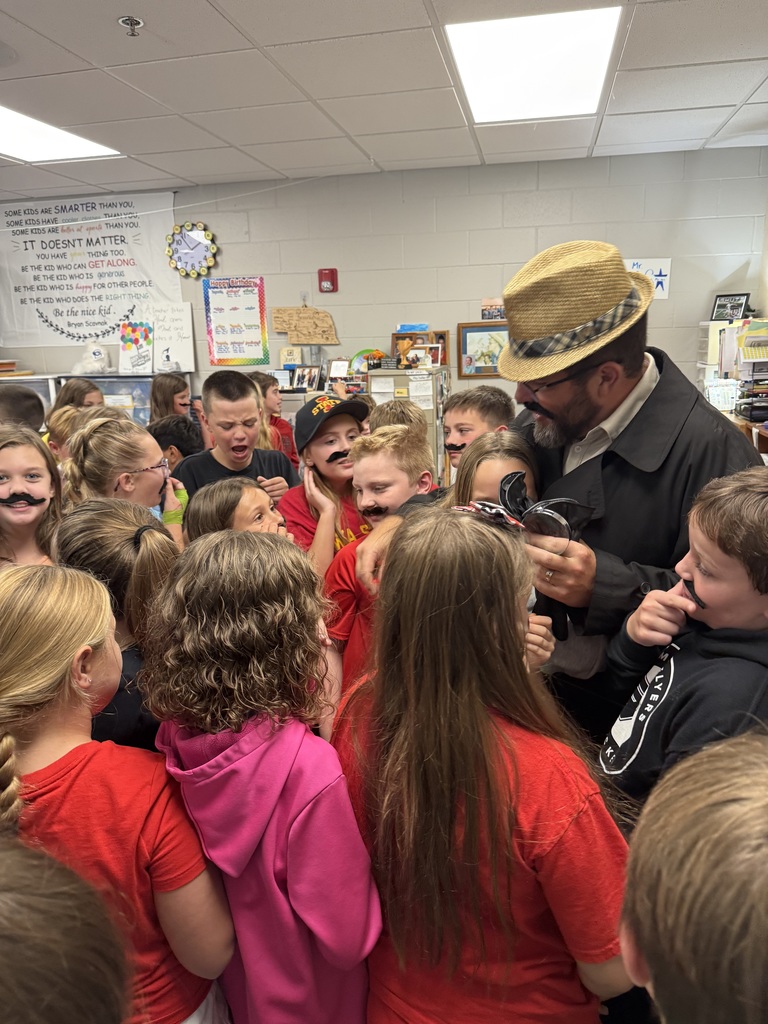 Group of students standing around a man wearing a hat and a fake mustache.
