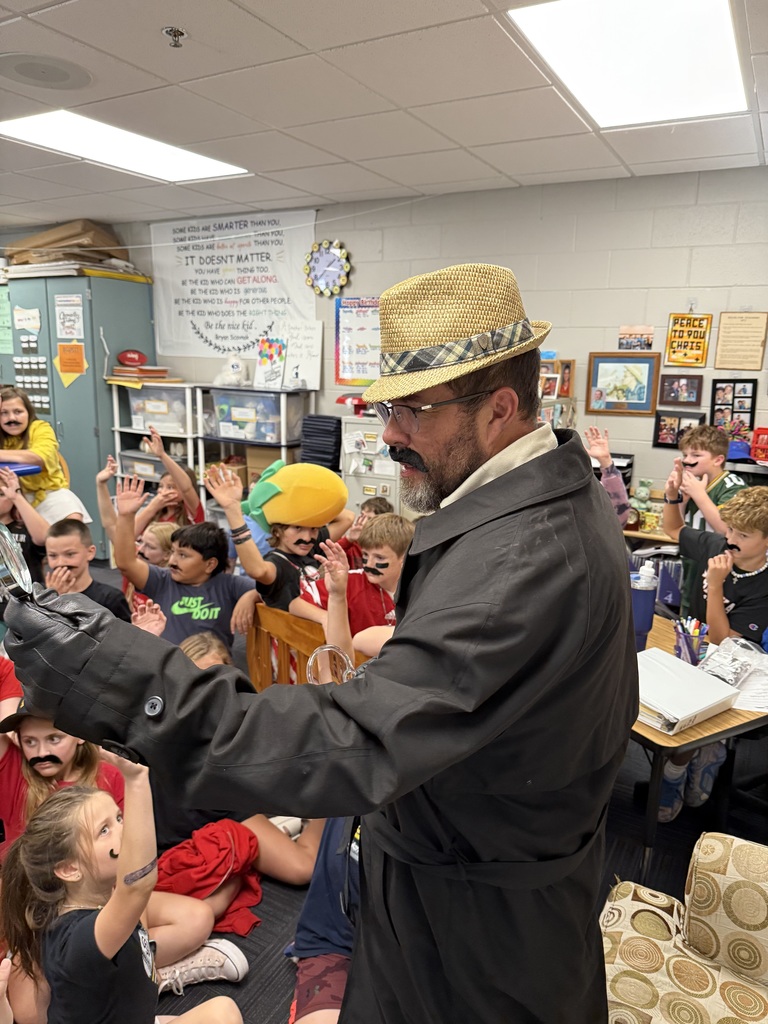 Group of students standing around a man wearing a hat and a fake mustache.