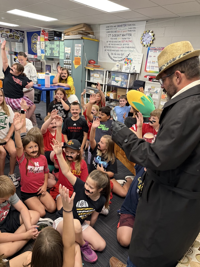 Group of students standing around a man wearing a hat and a fake mustache.