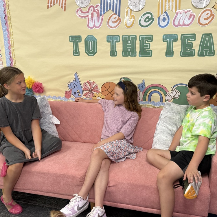 Three students sit on a pink couch talking