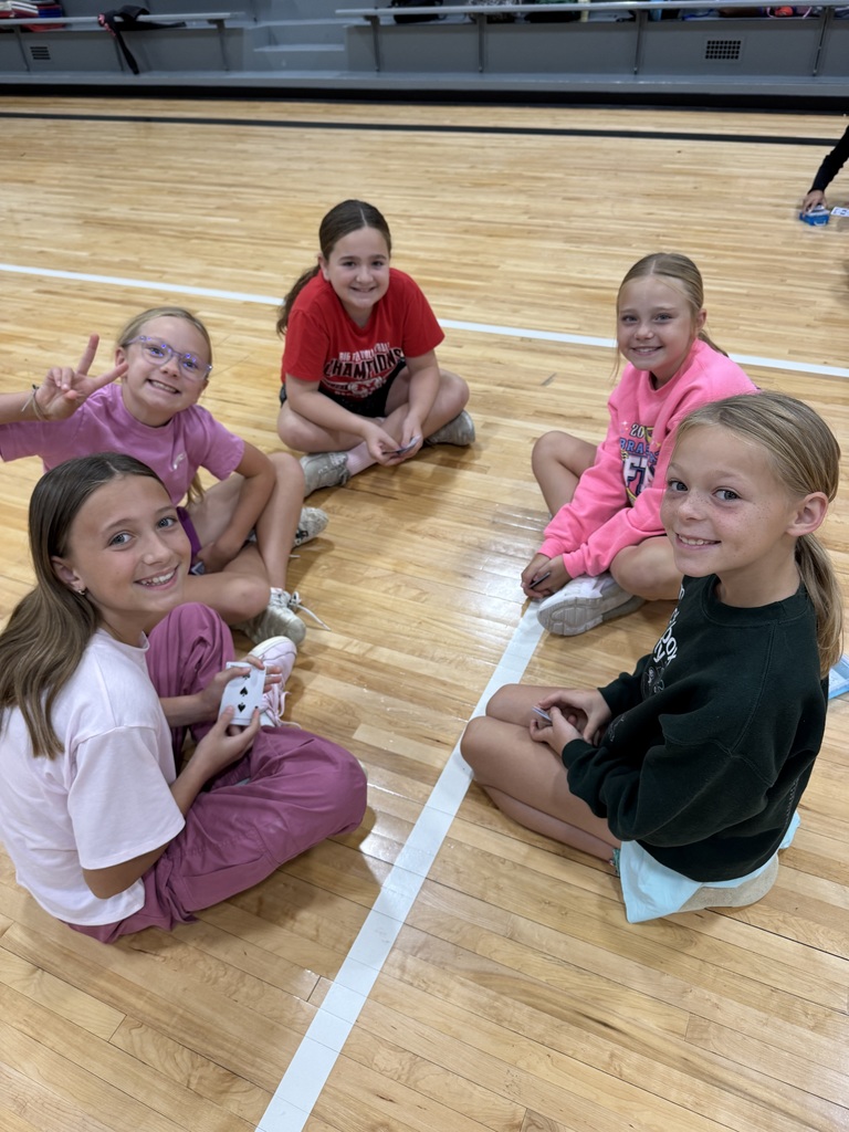 Group of students sitting on a gym floor with playing cards in their hand.