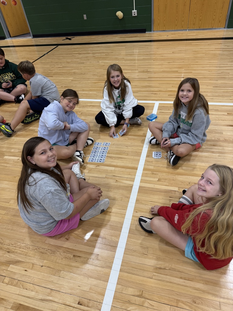 Group of students sitting on a gym floor with playing cards in their hand.