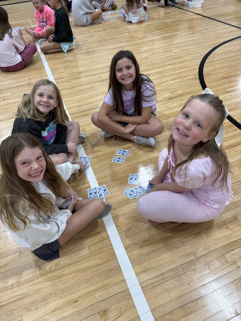 Group of students sitting on a gym floor with playing cards in their hand.