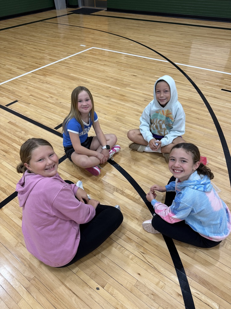Group of students sitting on a gym floor with playing cards in their hand.