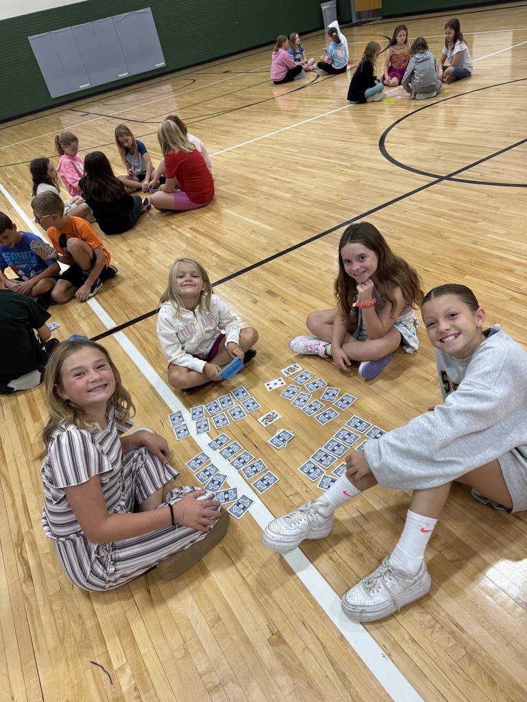 Group of students sitting on a gym floor with playing cards in their hand.