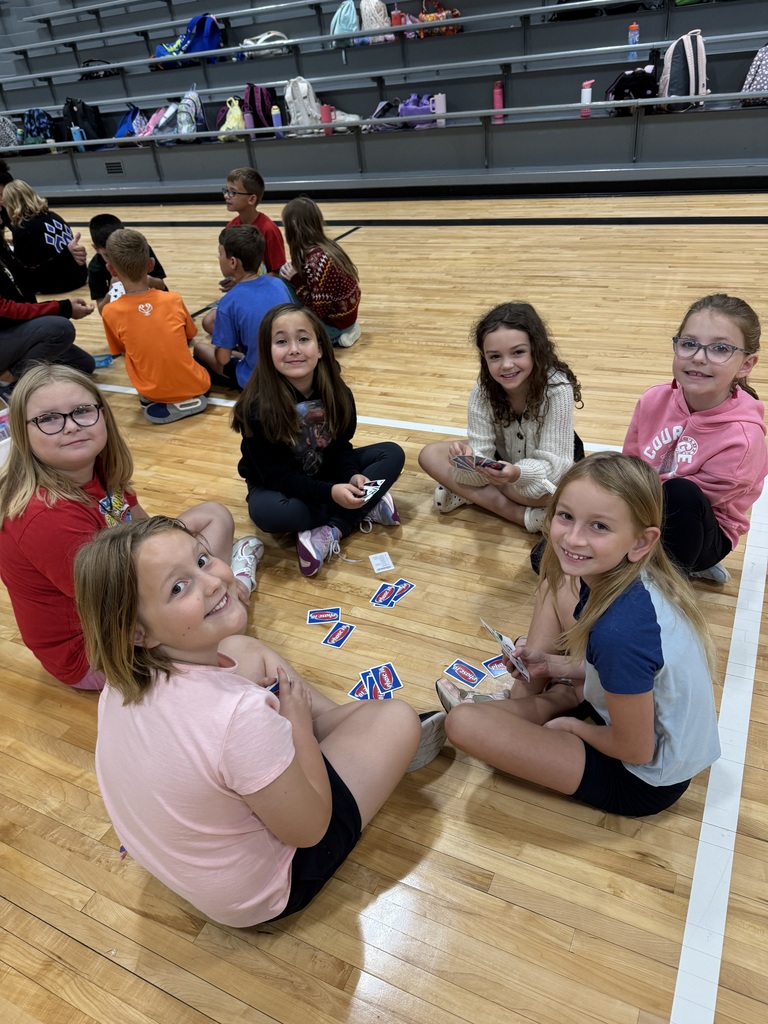 Group of students sitting on a gym floor with playing cards in their hand.