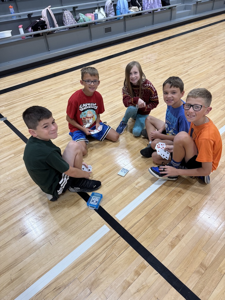 Group of students sitting on a gym floor with playing cards in their hand.