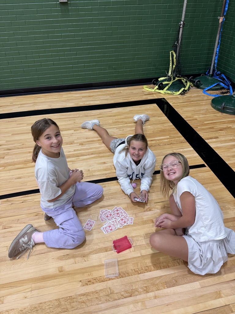Group of students sitting on a gym floor with playing cards in their hand.