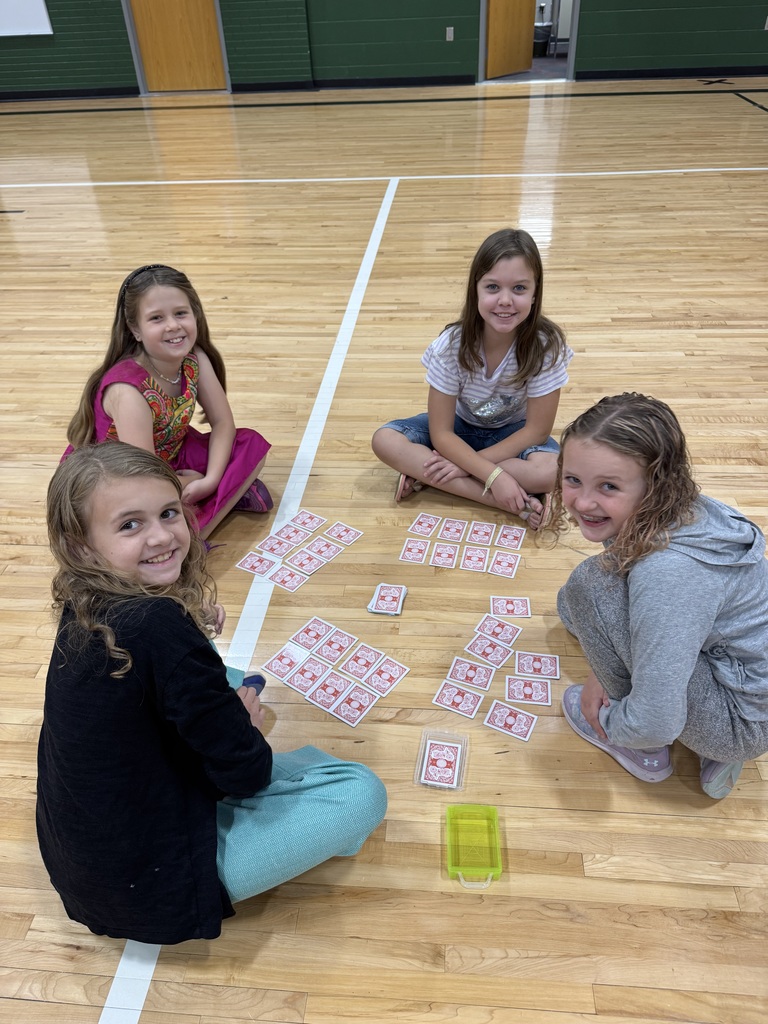 Group of students sitting on a gym floor with playing cards in their hand.