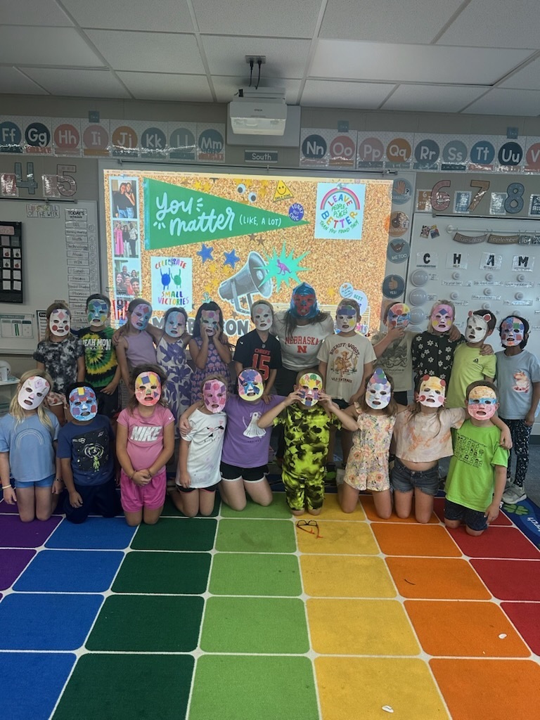 students posing on a classroom carpet with masks