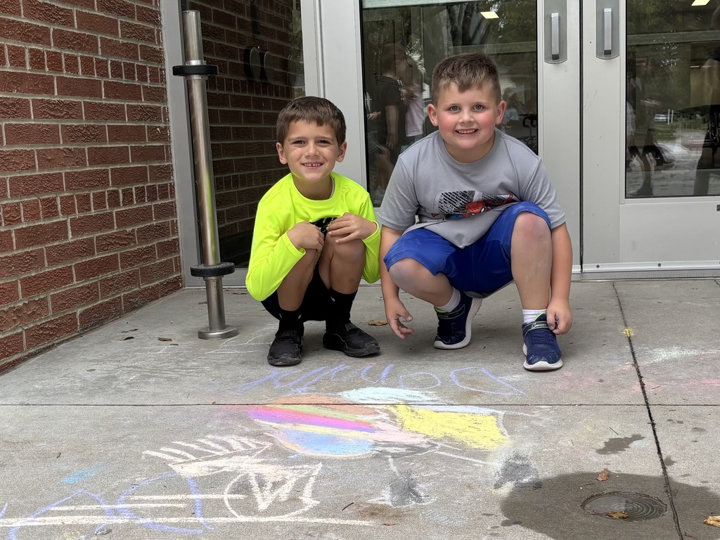 Two boys crouching on sidewalk looking at camera in front of drawing made by chalk.
