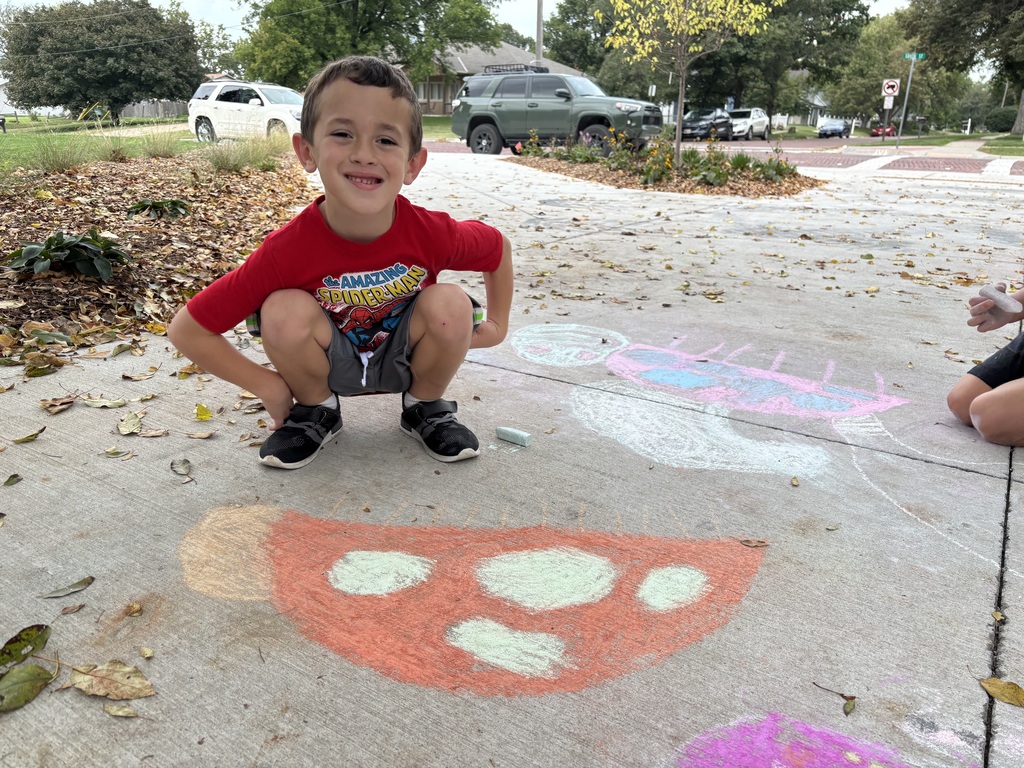 Boy standing on sidewalk looking at camera in front of drawing made by chalk.