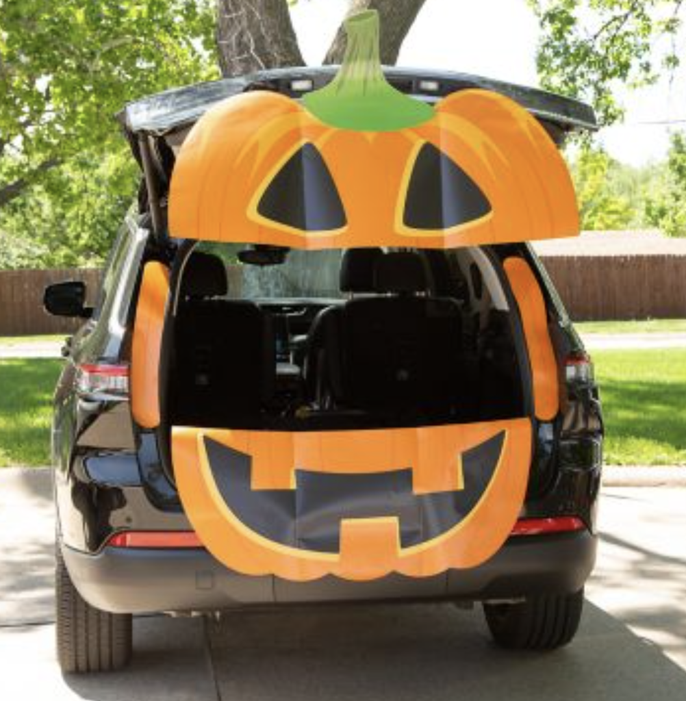 Car with trunk open with a giant pumpkin face.