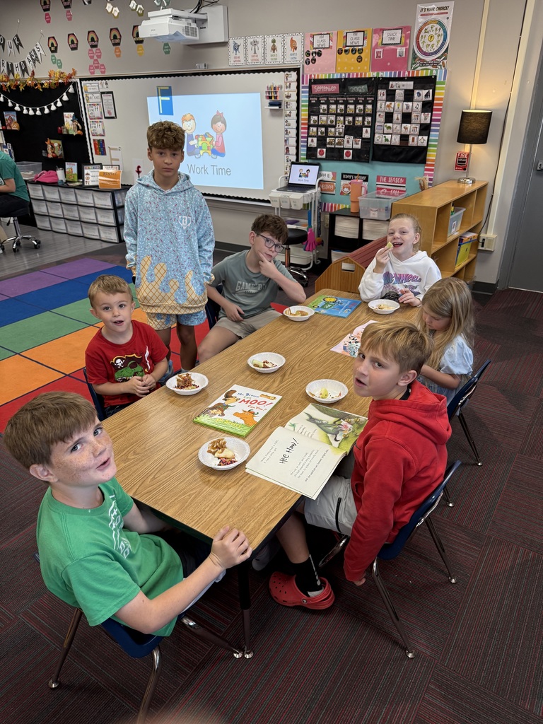 Group of students sitting around a large table with books and apples in front of them smiling.