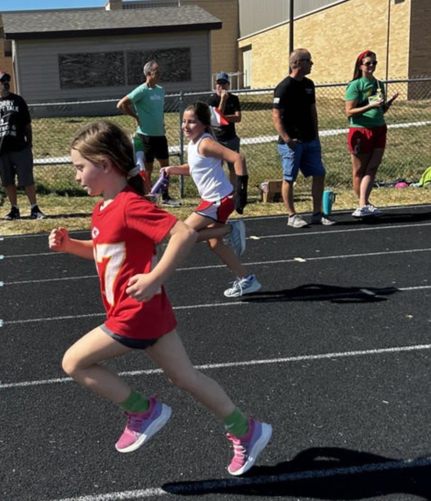 Two girls running on a track with people watching in the background.