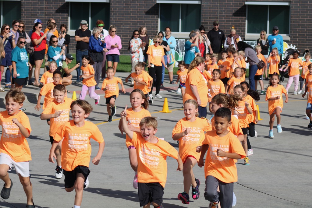 A group of first graders running in bright orange shirts