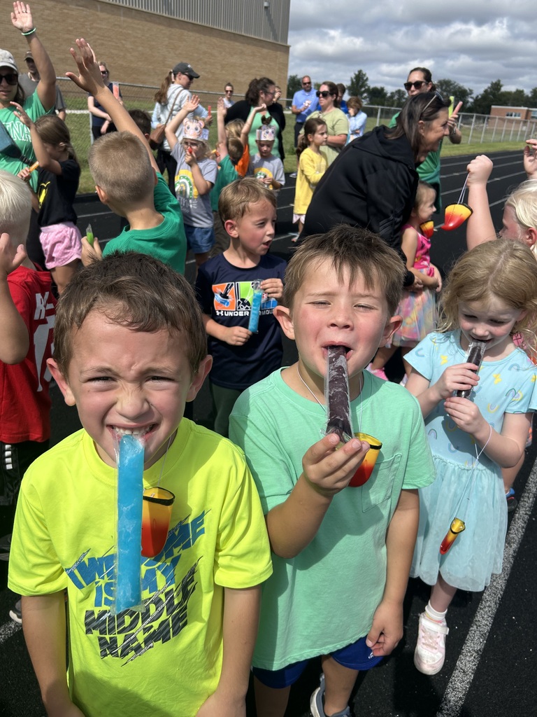 Three kids wearing colorful shirts smiling while eating popsicles.