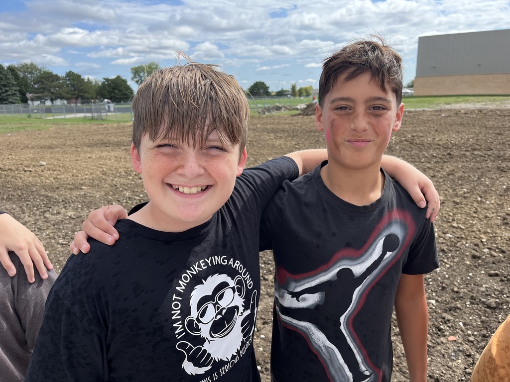 Two boys wearing black t shirts smiling while having their arms around each other.