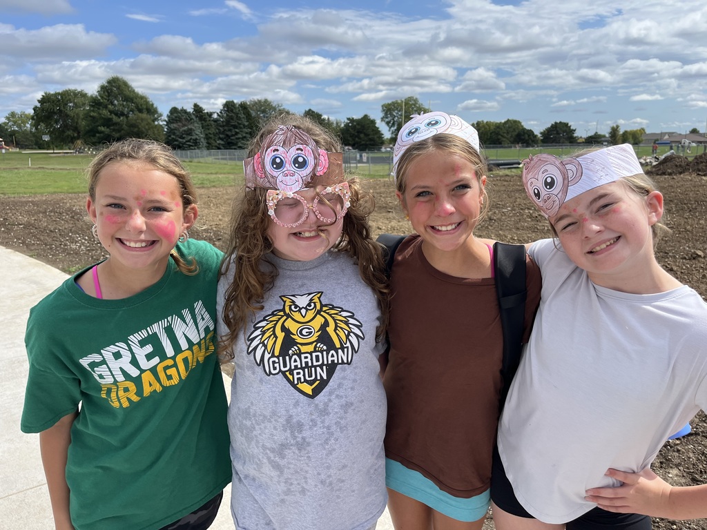 Four girls with their arms wrapped around each other.  Two of them are wearing paper monkey headbands.