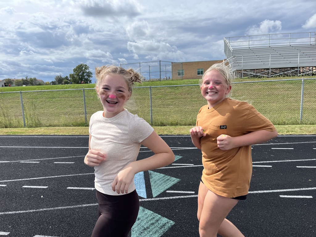 Two girls smiling while wearing face paint running around a track.