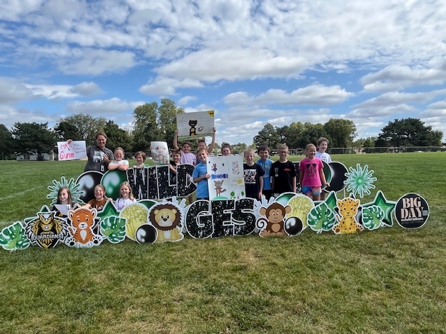 Group of students and their teacher in front of a Wild about GES sign. Some hold posters.
