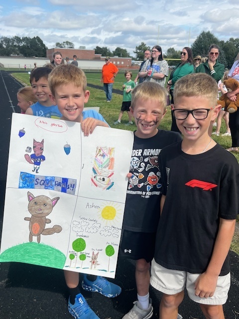 Four boys smiling while holding up a poster drawn of squirrels.