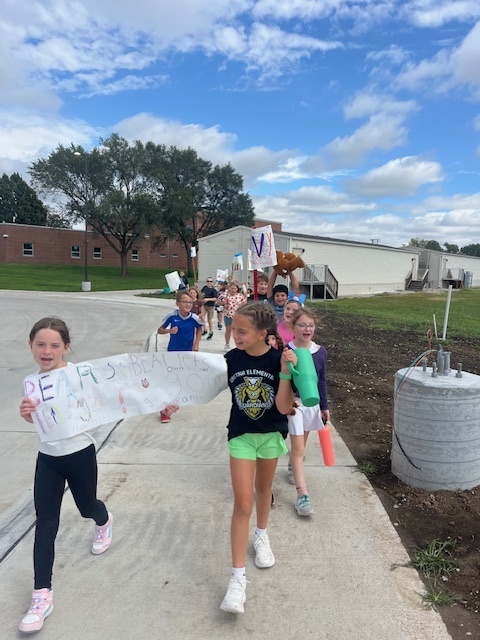 Group of students walk on a sidewalk with two in the front holding a sign that says Bears.