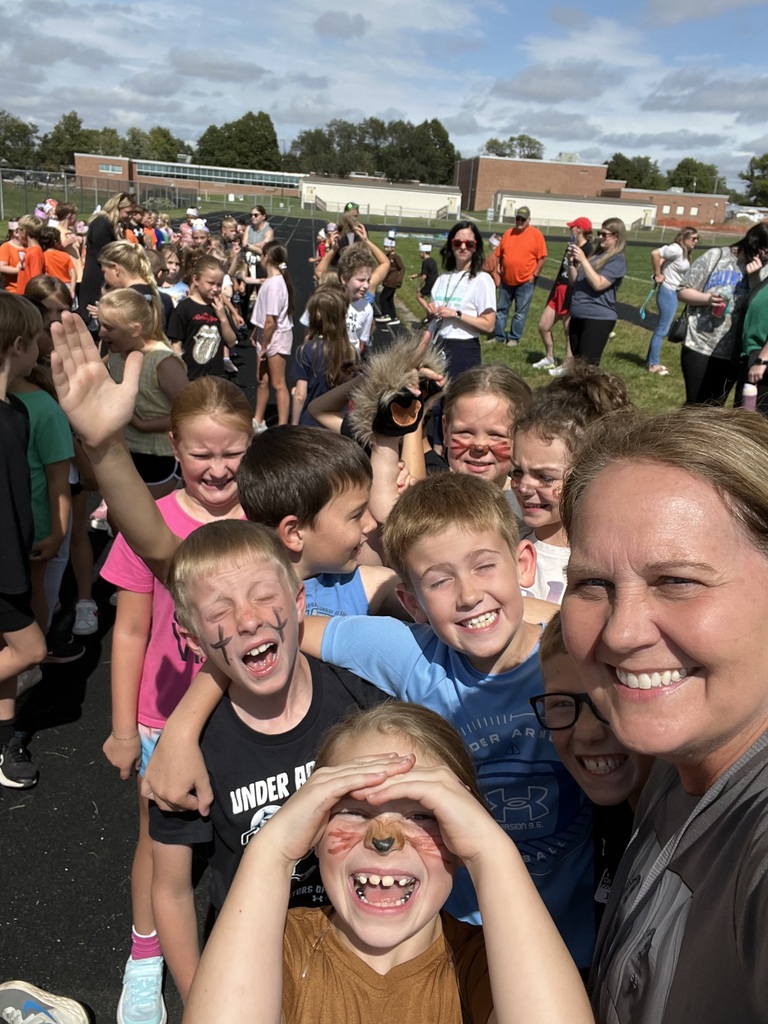 A teacher and a group of students smiling while squinting looking at camera.