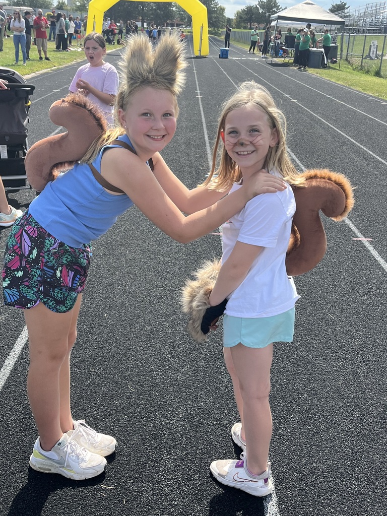 Two girls smiling while wearing squirrel tails and ears while standing on a running track.