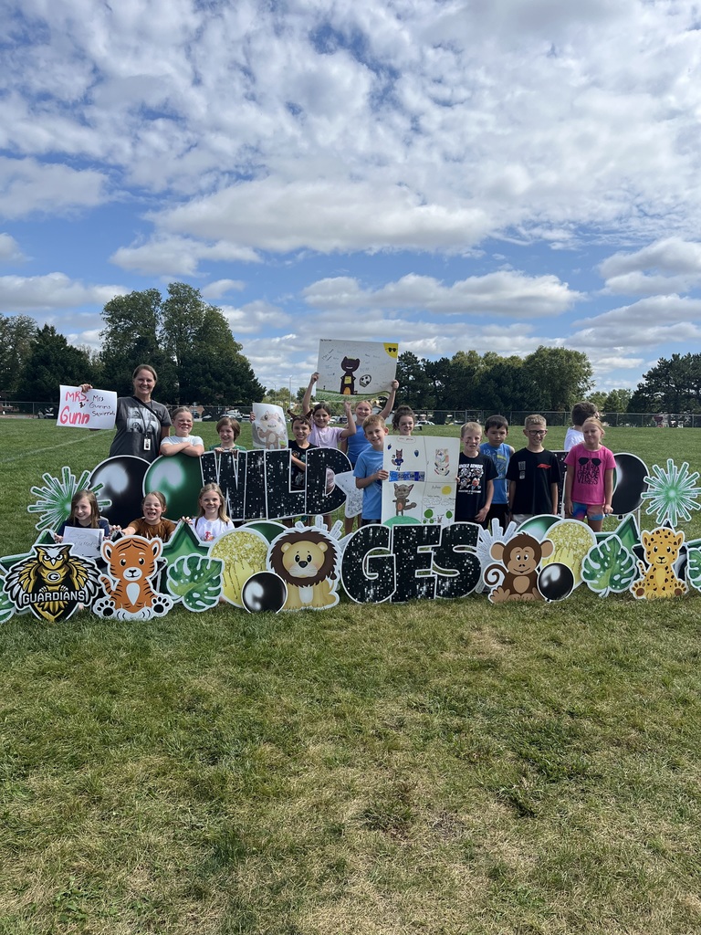 Group of students and their teacher posing behind a yard sign that says Wild About GES.