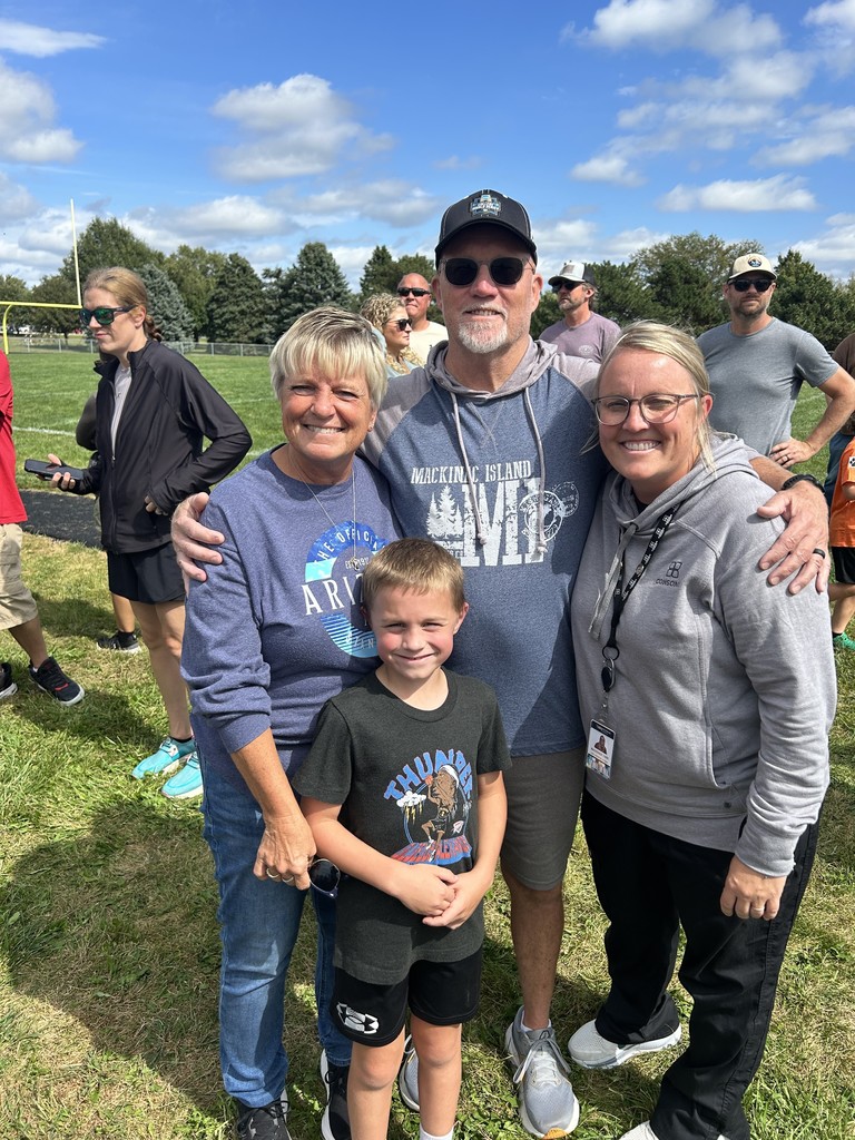 A boy standing with three adults smiling with other adults standing in the background.