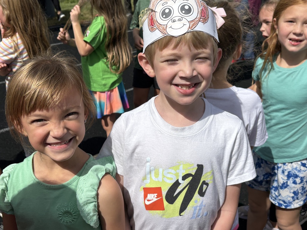 Two students smiling while standing on a running track with one of the students wearing a monkey paper headband.