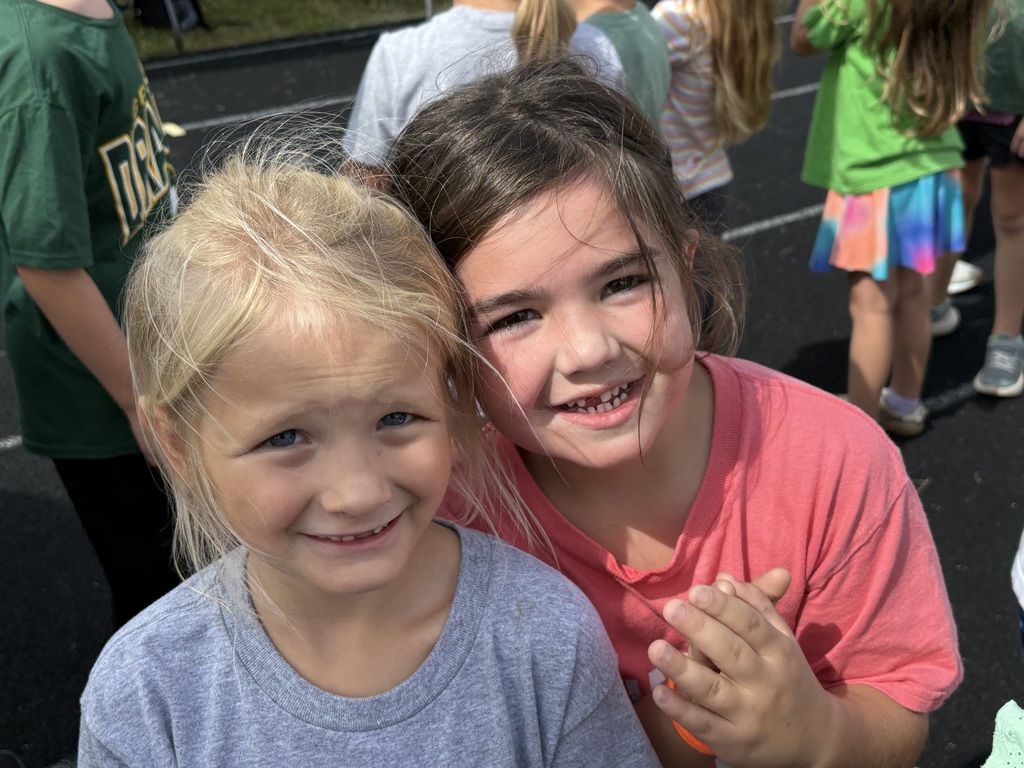 Two girls standing on a running track while smiling at the camera.
