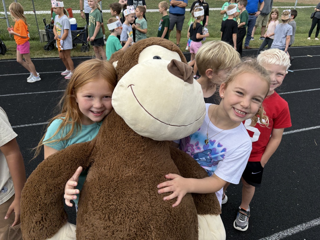 Group of students standing on a running track with two holding a large monkey.