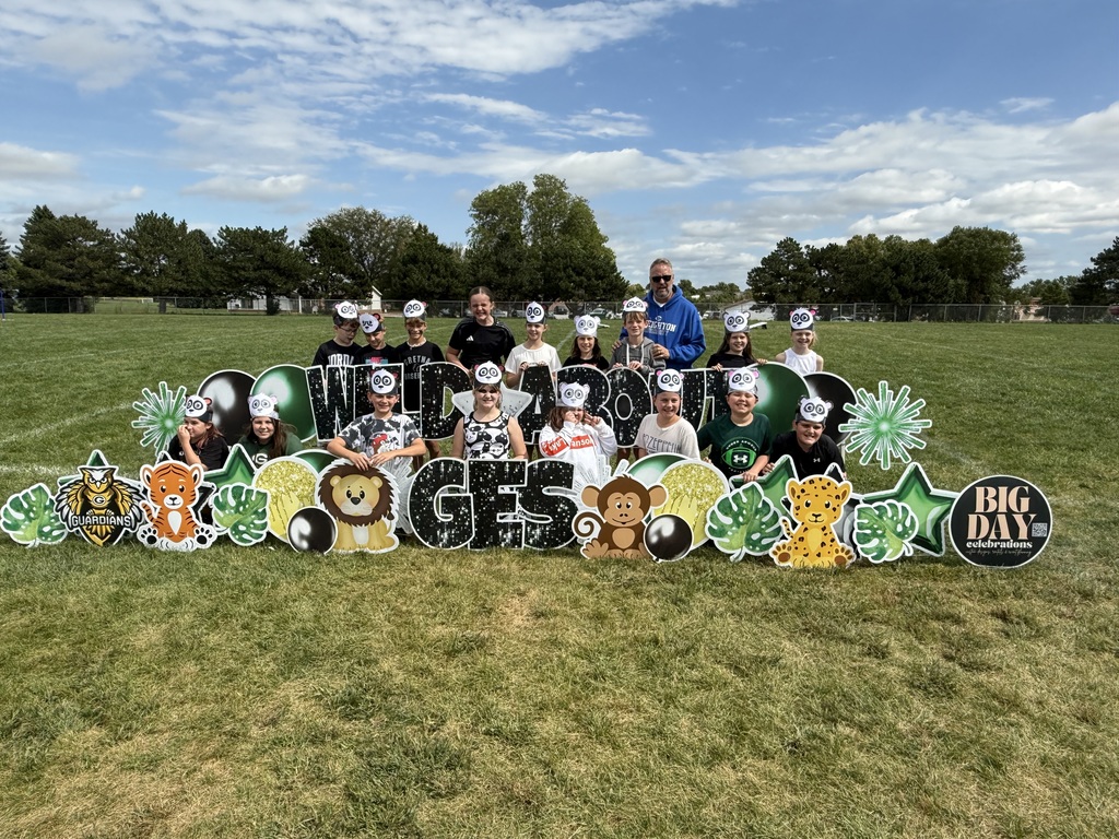Group of students standing in a grass field in front of a sign that says Wild About GES with animals signs present.