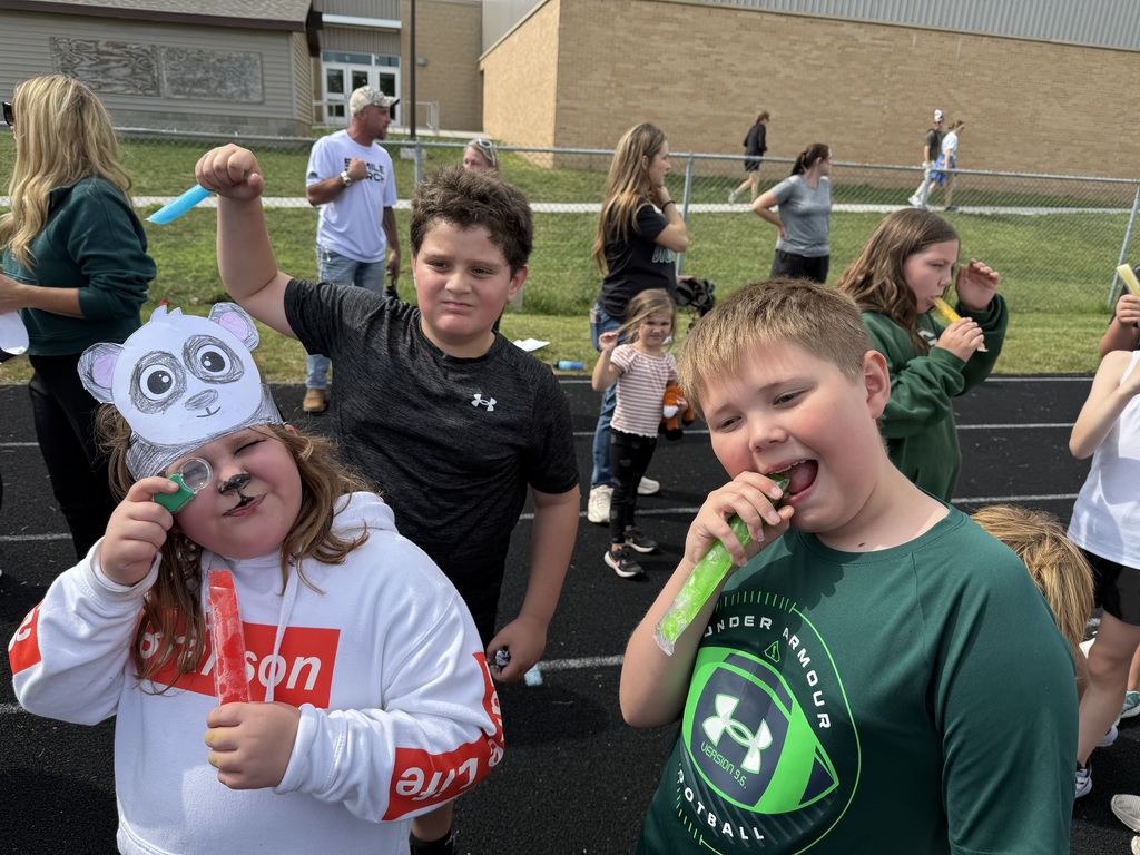 Three students standing on a track holding popsicles with one wearing a paper headband of a panda.
