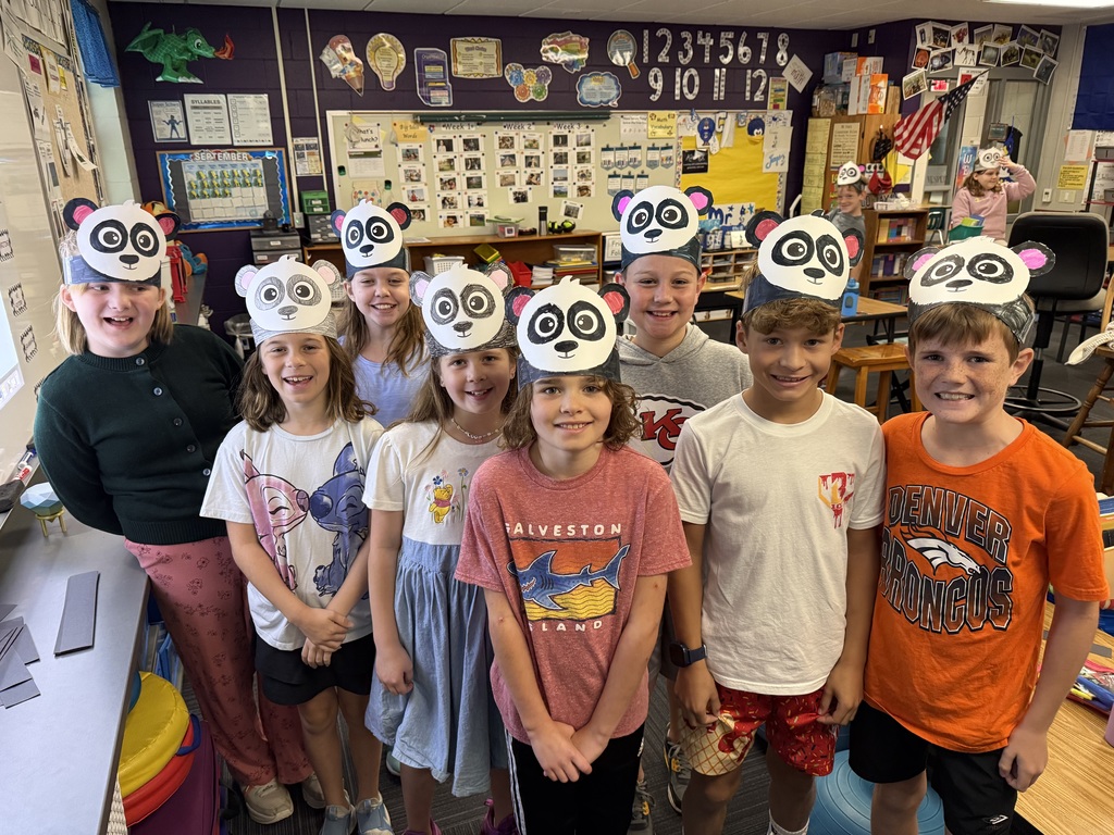 Group of students standing in a classroom with panda paper headbands.