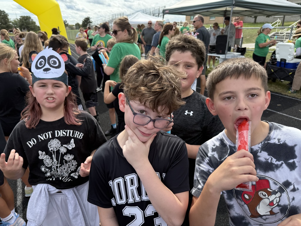 Group of students standing on a running track with one girl having a paper headband of a panda and one boy eating a popsicle.