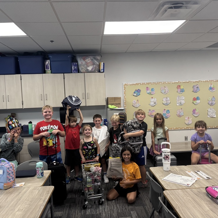 second graders holding objects like a shopping cart, garbage bag and suitcase for their “backpacks"