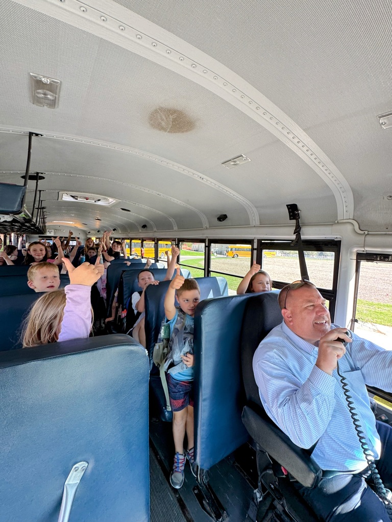 Bus full of elementary students giving a thumbs up as Superintendent Lightle speaks to them from the driver seat