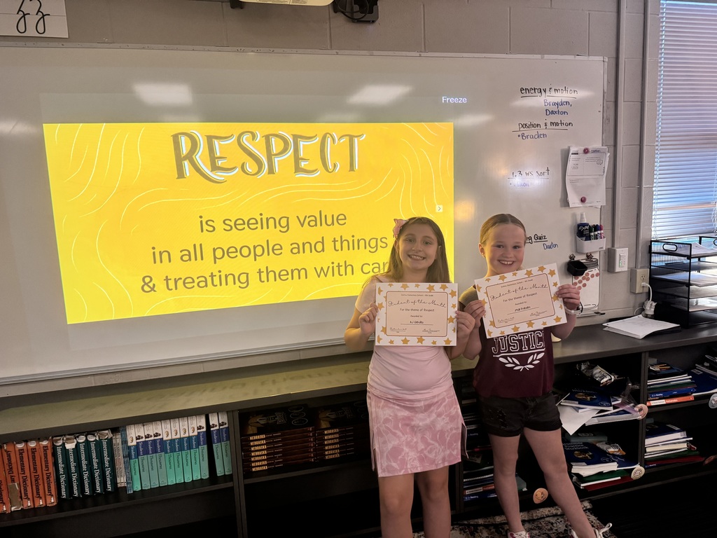 Two girls standing in front of a whiteboard with the phrase "Respect is seeing value in all people and things and treating them with care".