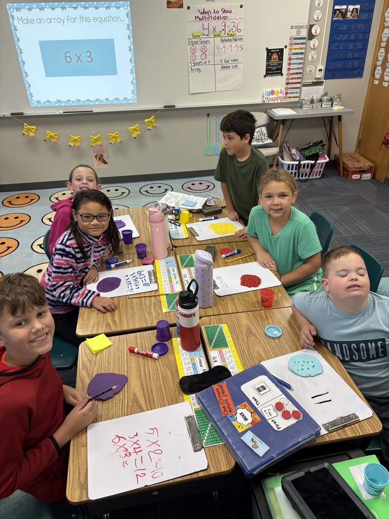 6 students sitting a table with whiteboards present and play dough visible. Students have multiplication problems on white boards.