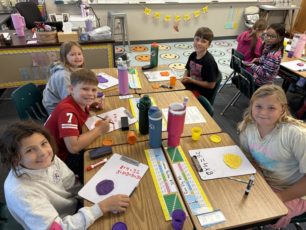 6 students sitting a table with whiteboards present and play dough visible. Students have multiplication problems on white boards.