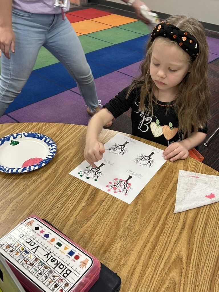 Girl sitting at a table decorating a paper with thumbprints of apples.