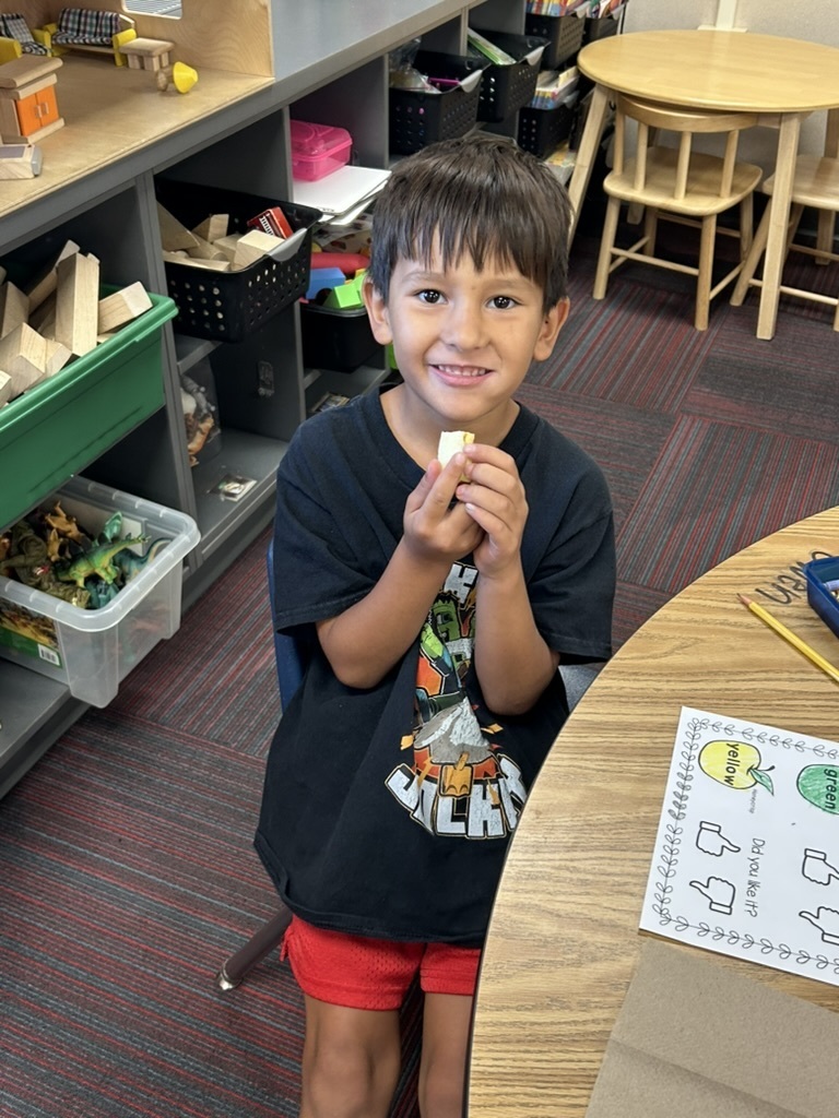 Boy sitting at a table smiling while eating an apple.