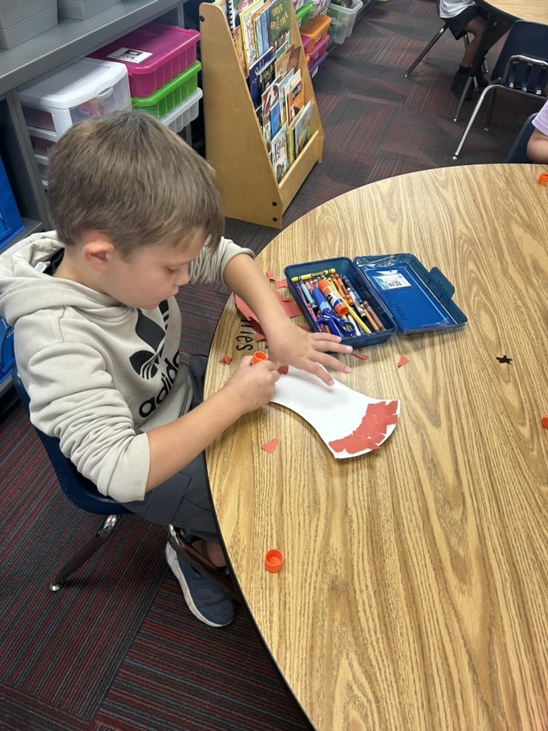 Boy working at a table with his pencil box open with a craft apple project.